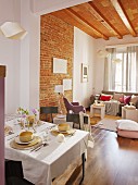 Breakfast table in open-plan interior; lounge area below wood-beamed ceiling in background