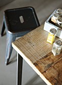 Jars of herbs in partially visible crate on wooden table with retro metal stool in background