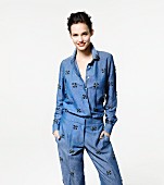 Brunette woman wearing pale denim shirt and trousers with appliqué pattern