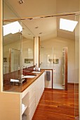 Designer bathroom - fitted washstand with white base units and glass shower cubicle below skylight