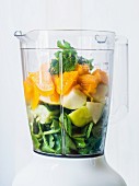 A green smoothie being made with fresh fruit and leaves