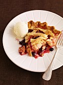 A slice of apple and berry pie with a scoop of vanilla ice cream