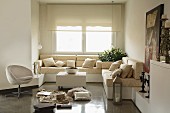 Sofa combination with beige upholster on platforms in window niche with roller blinds; retro easy chair and collection of various items on polished concrete floor