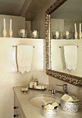 Antique mirror with silver frame above washstand with oval undermount sink decorated with soaps in silver boxes and candles