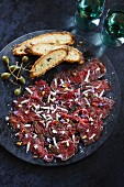 Beef carpaccio with pine nuts, grated cheese, edible flowers, capers and bread