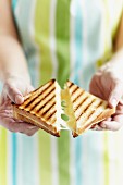 A woman breaking an toasted cheese sandwich in two
