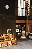 Double-height loft apartment with collection of spirits in crate-style shelving; gymnastic rings hanging form iron mezzanine balustrade and antique armchairs in corner