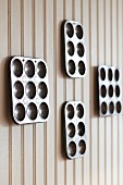 Four metal muffin trays of various sizes on light brown wooden wall