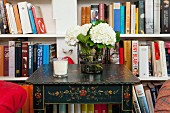 Hortensienstrauss auf Beistelltisch mit floraler Bauernmalerei, dahinter ein eingebautes Bücherregal