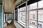 Giebelfensterfront in Dachbadezimmer mit Blick auf gegenüberliegende Straßenfassaden; im Hintergrund ein WC im Kniestockbereich