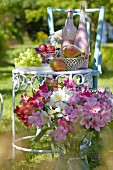 Blumenstrauss vor nostalgischem Metall-Gartentischchen gedeckt mit Früchten & Flaschen