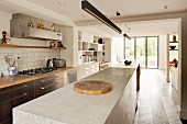 Long concrete kitchen counter under rod-shaped pendant lamps opposite kitchen counter with gas cooker