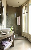 Curved, grey washstand with white basin in front of tiled shower area