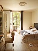 Double bed with floor-length bedspread next to open balcony door; console table and rattan chair in foreground