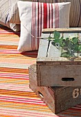 Vintage Holzkisten, gestapelt und Kissen mit gestreiftem Bezug auf gestreiftem Teppich