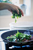 Hands adding wild garlic to a pan