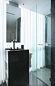 Column washstand with mirror suspended from ceiling and shower cubicle in front of glass wall with curtain