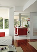 View from interior with exotic wood parquet through open sliding door into kitchen with red, central island counter