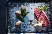 Beef steak, garlic, spices, herbs and potatoes on a baking tray