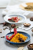 Turmeric powder, a dried chilli pepper, shiitake mushrooms and star anise on a table in front of a kitchen window