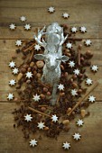 A stag figurine surrounded by nuts, cinnamon stars, cinnamon sticks and star anise