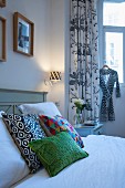 Colourful scatter cushions on bed in front of black and white patterned curtains