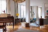 Offener Wohnraum mit antikem Klavier, hinter Stütze Loungebereich mit verschiedenen Sofas