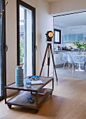 Ein Lowboard auf Rollen und eine Dreibein-Lampe im Industrie-Stil, Blick in die Küche mit Esstisch