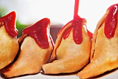 Ketchup being poured over samosas