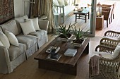 Pale couch and rattan armchairs around wooden coffee table adjoining terrace with open sliding door