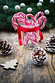 Candy canes in a glass with pine cones on a wooden surface