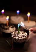 Frau zündet Geburtstagskerzen auf festlichen Cupcakes an