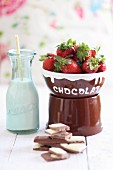 Milchschokolade, frische Erdbeeren und Milchflasche (Zutaten für Schokoladenfondue)