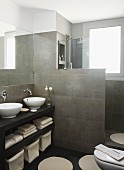 Wooden washstand with twin countertop basins in front of tiled partition screening walk-in shower