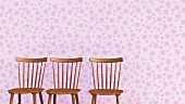 Drei Holzstühle vor fliederfarbener Tapete mit Blütenmuster