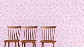 Three wooden chairs against lilac wallpaper with floral design