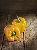 Two yellow peppers on a wooden surface
