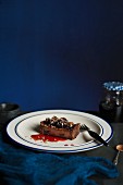 A slice of dark chocolate and cherry tart on a white plate with a blue rim and fork