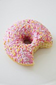 A pink iced doughnut with sugar sprinkles and a bite taken out