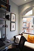 Antique couch with pale upholstery in front of arched window; modern desk integrated into metal shelving