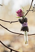Rose in Reagenzglas mit Deko geschmückt an einem Zweig aufgehängt