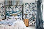 Doppelbett mit gepolstem Kopfteil unter blaugrau gestreiftem Baldachin in Schlafzimmer mit blauer Blumentapete