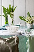 White place setting, lily of the valley and pastel green tablecloth on table outdoors