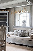 Old couch with upholstery and cushions in various shades of grey below window