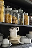 White crockery and storage jars in open-fronted, wall-mounted cabinet