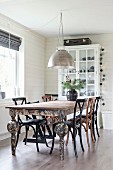 Wooden chairs around dining table with peeling paint below metal pendant lamp in dining area with white, wood-clad walls