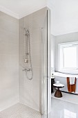 Bodenebene Dusche mit Glastür, im Hintergrund Beistelltisch vor Badewanne am Fenster, in modernem Bad mit Vintage Flair