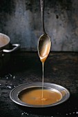 Homemade caramel sauce dripping from a spoon onto a metal plate