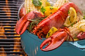 Steamed lobster in a pot with corn cobs, potatoes, lemons, coriander, rosemary and spices