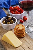Cheddar cheese, crackers, Kalamata olives, tomatoes and a glass of red wine on a rustic wooden table